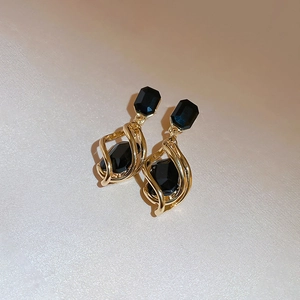 Close-up of vintage gold geometric earrings with black crystals on fabric background