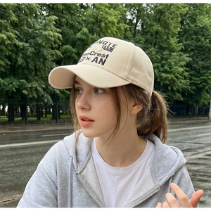 Outdoor close-up of a cream cotton baseball cap with black artistic embroidery detailing