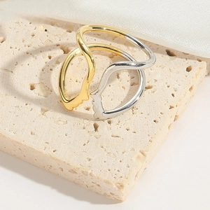 Close-up of minimalist gold and silver face outline rings on a beige stone surface