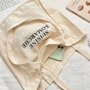 Detailed view of canvas tote bag outer pocket holding a phone with letter print