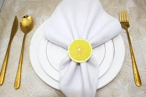 Close-up of a lifelike lemon slice napkin ring with white linen on gold-rimmed tableware