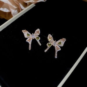Macro shot of gold butterfly earrings with white zircons and green gemstones on black velvet