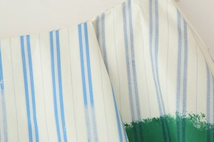 Close-up of white fabric with blue vertical stripes and green dye patterns at the bottom hem