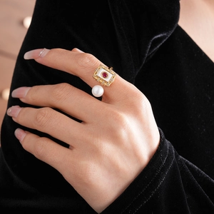 Close-up of gold plated ring featuring a square white pearl and a red gemstone inlay