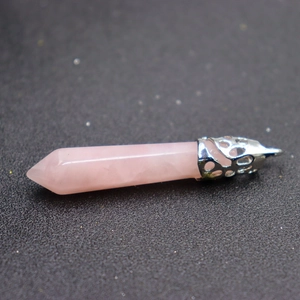 Pink quartz hexagonal crystal pendant with ornate silver metal filigree cap on dark surface