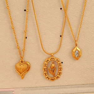 Trois colliers dorés avec pendentifs cœur, tulipe et zircon sur un support à bijoux