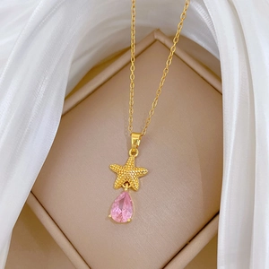 Detailed shot of a gold starfish necklace with pink teardrop gemstone on silk fabric