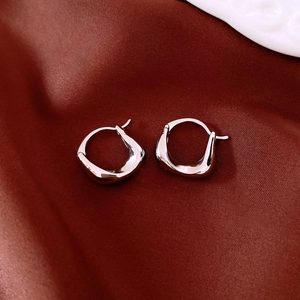 Macro detail of silver geometric drop earrings on luxurious dark red satin fabric