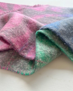Gros plan sur la texture d'une écharpe à carreaux avec pompons roses et bleus et tissage