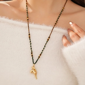 Detail van een gouden pony hanger ketting met tijgeroog kralen op een witte trui