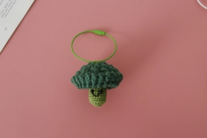 Detail of a handmade crochet broccoli pendant with a smiley face on a pink background