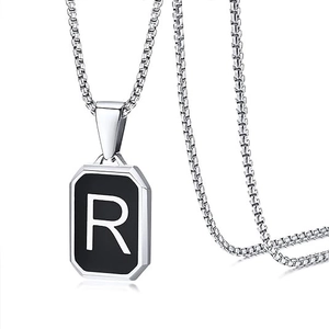 Detail of a square black pendant featuring a silver letter R on a stainless steel chain
