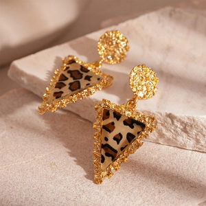 Macro detail of golden hammered metal earrings with triangular leopard print resin