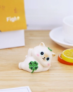 Detail of cute white lucky cat figurine holding a green four-leaf clover on a desk