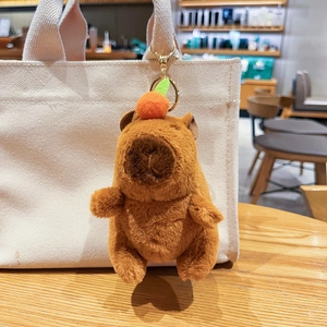 Cute Capybara plush keychain hanging on a beige canvas bag in a cozy cafe setting