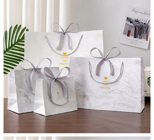 Detail of marble pattern gift bags with grey ribbon handles and gold foil lettering