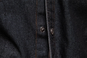 Détail macro du tissu denim indigo foncé avec bouton-pression en métal et coutures orange vif