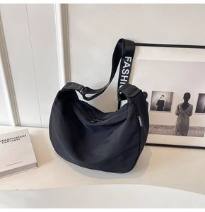 Detail of waterproof black nylon crescent bag with wide strap and zipper on white surface