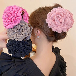Detailed view of oversized fabric flower hair clips in pink, grey, and black colors