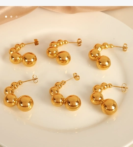 Detailed view of golden beaded C-shaped hoop earrings on a white ceramic plate