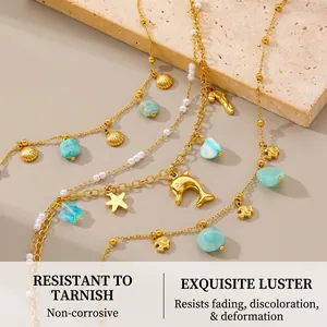 Detail of gold ocean-themed anklet set with shell star and dolphin charms on stone