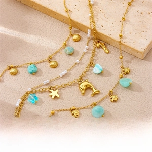 Detail of gold ocean-themed anklet set with shell star and dolphin charms on stone