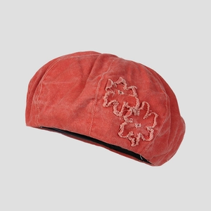Detail of washed red pumpkin beret with distressed cotton and floral patch embroidery