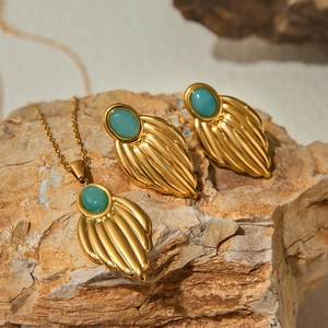 Elegant gold titanium steel jewelry set with green oval gemstones on a natural rock surface