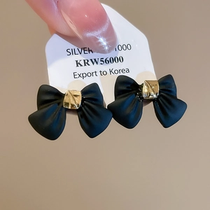 Detail of matte black bow earrings with gold trim on a silver needle display card