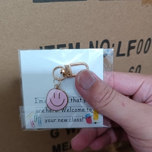 Pink enamel smiley face keychain with golden hook on a white welcome gift card