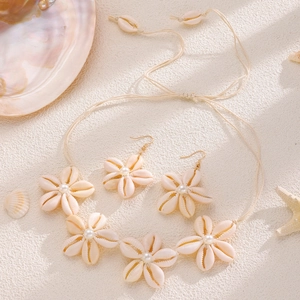 Set collana e orecchini in conchiglia naturale e perle con motivi floreali sulla sabbia