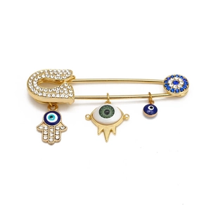 Detail view of golden Hamsa Hand and Evil Eye charms on a rhinestone safety pin brooch