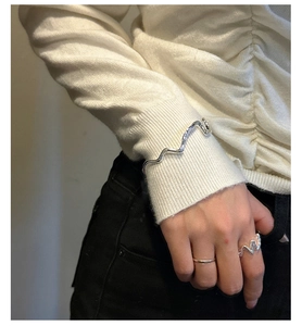 Detail of silver wavy open bangle and matching minimalist rings worn over a white sleeve