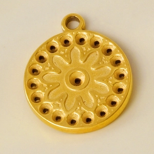Detailed close-up of golden round pendant with floral engraving and set holes in steel