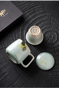 Three-piece celadon crackle glaze ceramic tea mug with strainer and lid on dark wood