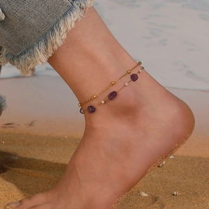 Gros plan d'une chevillère double rangée dorée avec pierres violettes sur la plage