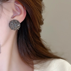 Détail d'une boucle d'oreille demi-sphère sertie de cristaux gris foncé portée par un mannequin