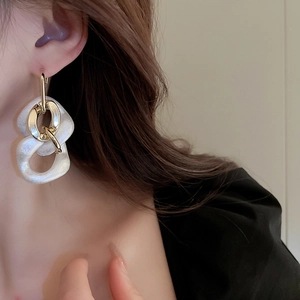 Close-up of geometric acrylic link earrings with pearl effect on a model's ear