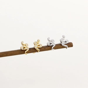 Detailed view of gold and silver snake earrings with zircon stones on a wood stand