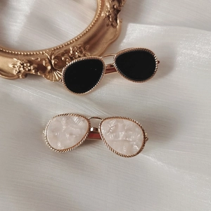Elegant sunglasses-shaped hair clips in black and pearlescent white on textured fabric