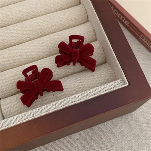 Macro shot of small burgundy velvet bow hair claws inside a cream-colored jewelry box