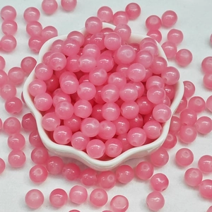 Close-up of translucent pink round glass beads in a white flower-shaped ceramic dish