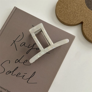 Dettaglio di un mollettone rettangolare in acetato bianco perlato sopra un libro decorativo