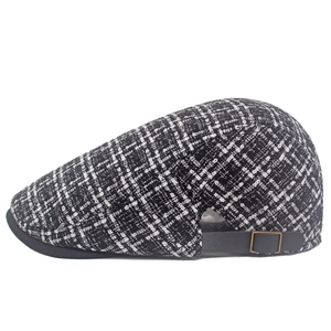 Dettaglio di un basco in tweed a quadri bianchi e neri con cinturino in pelle e fibbia in bronzo