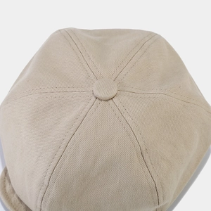 Macro view of beige twill cotton newsboy cap showing six-panel stitching and top button