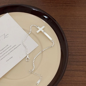 Elegant silver cross charm bracelet on a ceramic plate with a vintage card on wood table