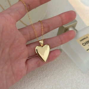 Hand holding a minimalist 18K gold plated heart pendant necklace with high mirror polish