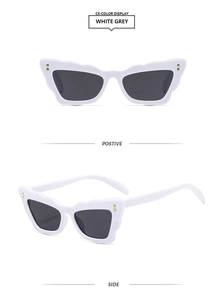 White cat-eye sunglasses with dark grey lenses and gold square studs on the frame