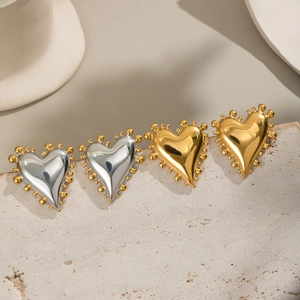 Détail de boucles d'oreilles cœur géométriques en or et argent sur pierre texturée