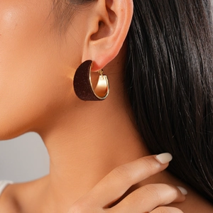 Close-up of C-shaped earrings with brown flocking and gold metal finish on a model